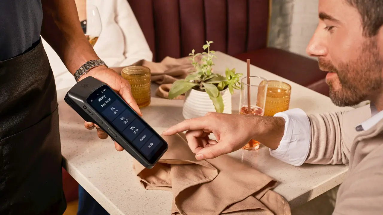 A server taking a card payment at a restaurant table with a handheld terminal